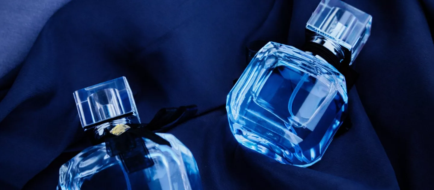 Two crystal-cut blue perfume bottles resting on dark navy blue silk fabric in dramatic moody lighting