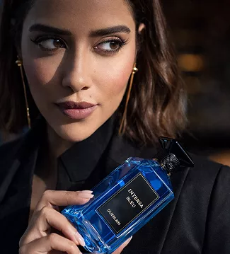 A woman in a black blazer holding a bright blue Guerlain Intensa Bleu perfume bottle, featuring a sophisticated and sharp aesthetic.