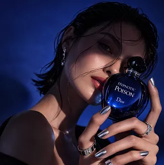 Woman with wet hair holding Dior Hypnotic Poison perfume bottle close to her face against a deep blue background