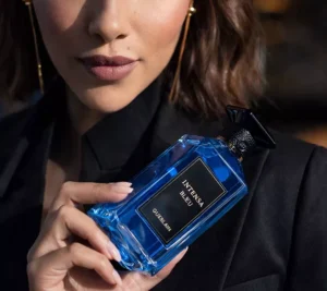 A woman in a black blazer holding a bright blue Guerlain Intensa Bleu perfume bottle, featuring a sophisticated and sharp aesthetic.