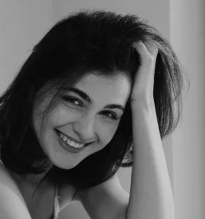 Close-up black and white photo of a woman laughing joyfully, running her hand through her voluminous dark hair.