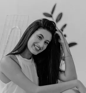 Black and white portrait of a woman with long hair smiling warmly, leaning her head on her hand against a minimalist background.